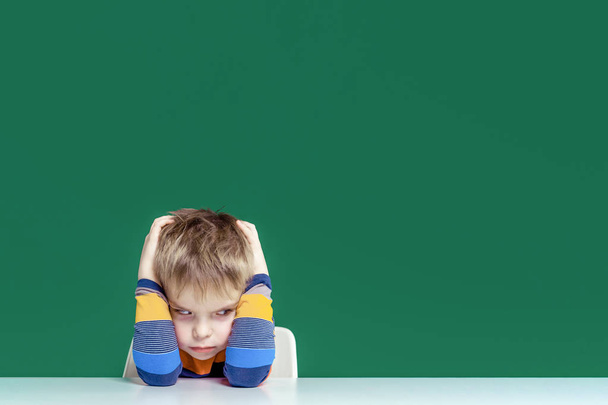 An angry boy sits at a desk holding his head. Copy space - Fotoğraf, Görsel