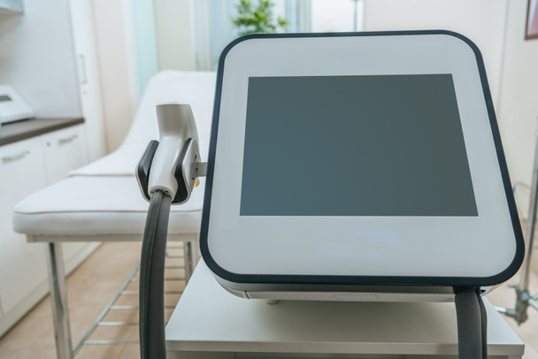 Máquina láser con pantalla en blanco cerca de sofá de belleza en la clínica
 - Foto, imagen