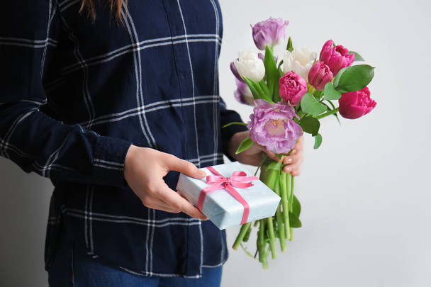 Woman with gift box and bouquet of beautiful flowers on light background - Fotoğraf, Görsel