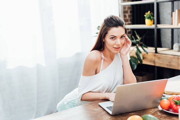 Attractive young woman using laptop at table in kitchen - Photo, image