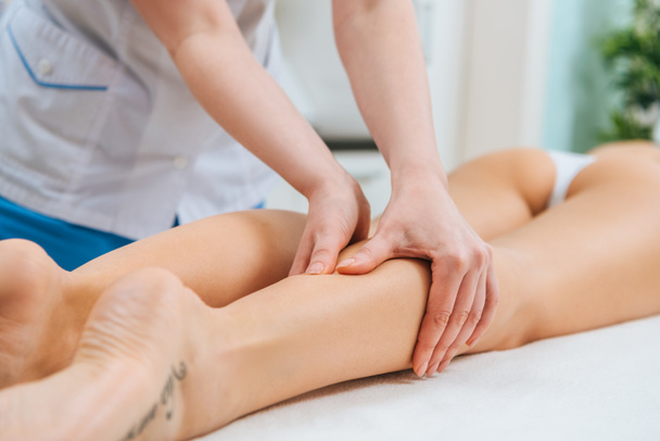 Vista cortada do massagista fazendo massagem nas pernas para a mulher na mesa de massagem
 - Foto, Imagem