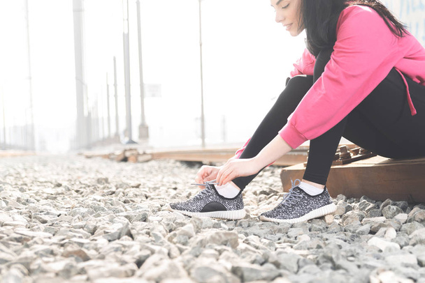Attractive young woman in sportswear tying shoelaces on her sneakers and getting ready for street workout - Φωτογραφία, εικόνα