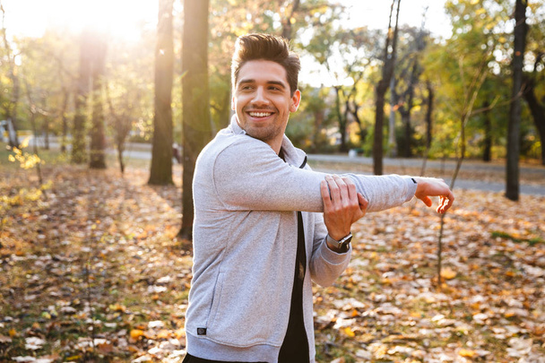 Handsome young sportsman outdoors in park listening music with earphones make exercises. - 写真・画像