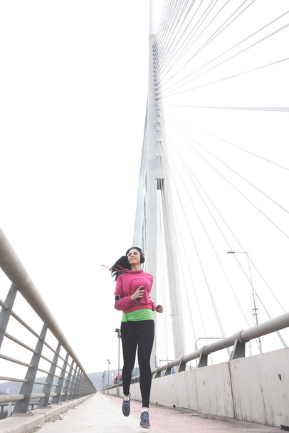 Attractive sporty brunette running on bridge full of energy - Foto, Bild