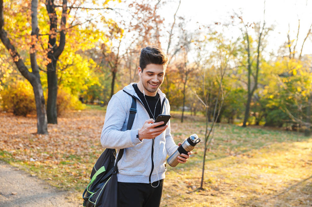 Sportowca na świeżym powietrzu w parku słuchania muzyki za pomocą słuchawek przy użyciu telefonu komórkowego. - Zdjęcie, obraz