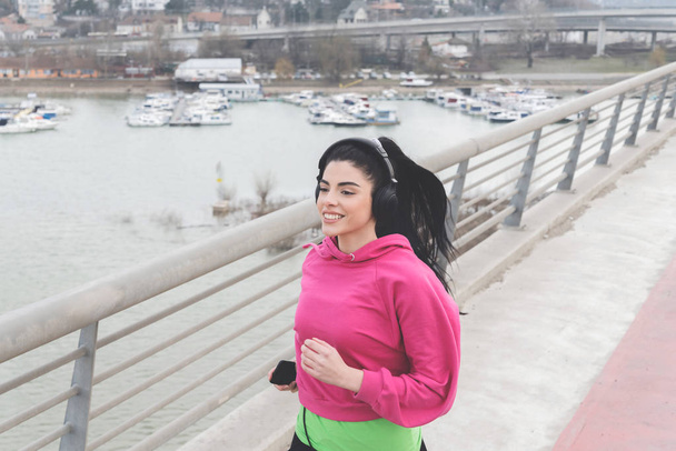 Portrait of attractive brunette with beautiful smile full of energy running by river in city - Φωτογραφία, εικόνα