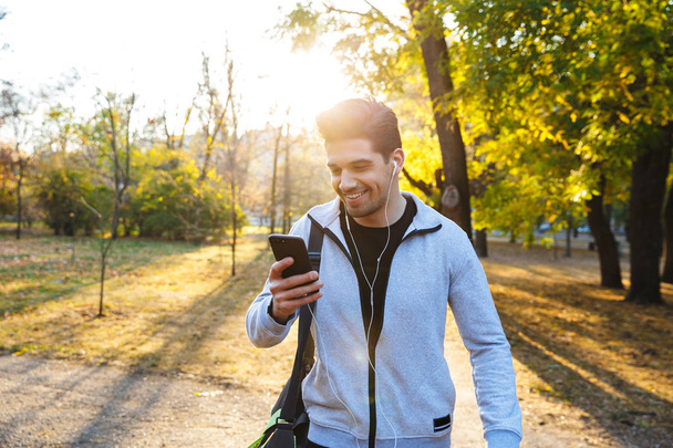 Sportsman outdoors in park listening music with earphones using mobile phone. - Фото, зображення