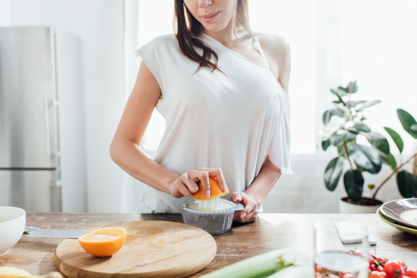 Частичный вид женщины, делающей свежий апельсиновый сок на кухне
 - Фото, изображение