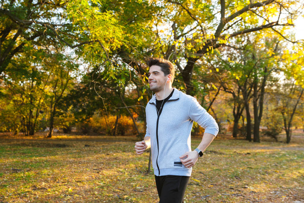 Young sportsman outdoors in park listening music with earphones running. - Fotografie, Obrázek