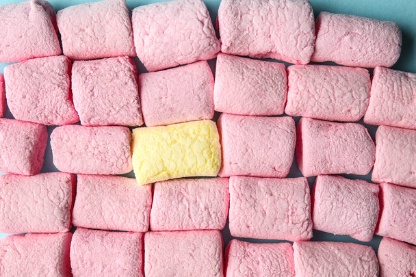 Um marshmallow amarelo entre os cor-de-rosa no fundo de cor, close-up. Conceito de singularidade
 - Foto, Imagem