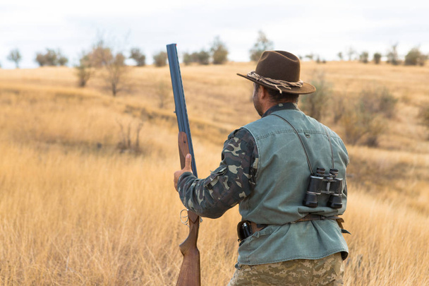 帽子と、草原で獲物を捜して銃ハンターが獲物を目指しています - 写真・画像