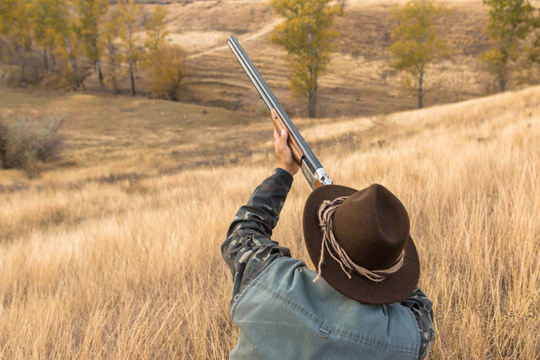 Caçador com um chapéu e uma arma em busca de presa na estepe, visa a presa
 - Foto, Imagem