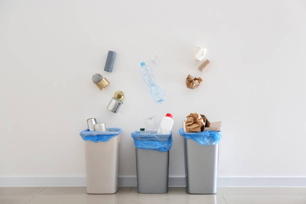 Śmieci wpadające do pojemników na śmieci w pobliżu białej ściany - Zdjęcie, obraz
