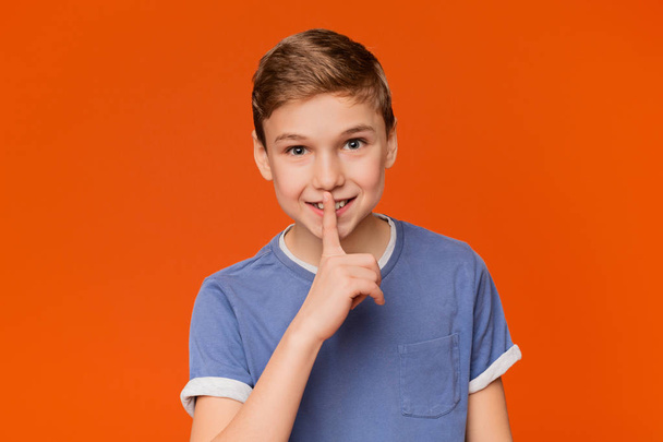 Young boy showing silence sign on orange background - Fotografie, Obrázek