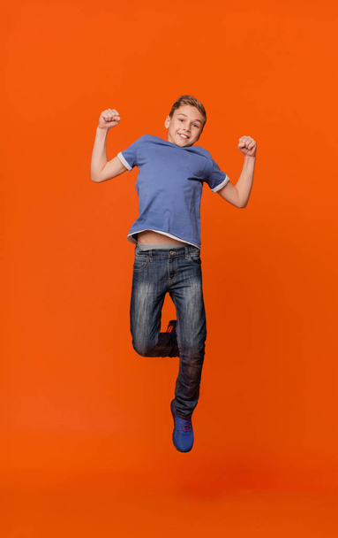 Happy schoolboy jumping for joy on orange - Фото, зображення