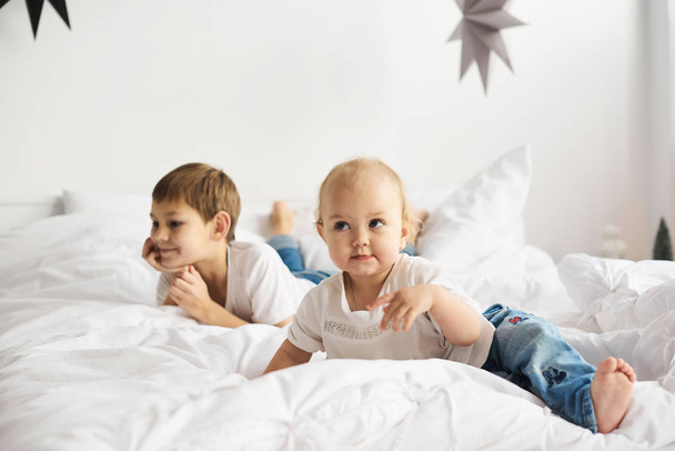 Happy kids playing in white bedroom. Little boy and girl, brother and sister play on the bed. - Foto, afbeelding