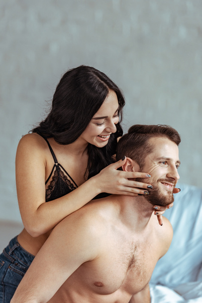 attractive woman and handsome shirtless man hugging and smiling in bedroom  - Φωτογραφία, εικόνα