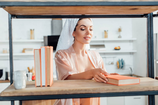 Curious woman in housecoat with towel on head holding book - Foto, imagen