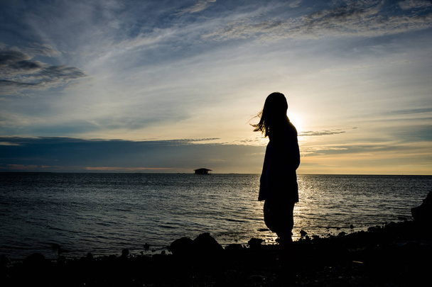 Silhouette d'une fille debout seule sur le bord de la mer avec un beau ciel en arrière-plan à Harapan Island, Indonésie
 - Photo, image