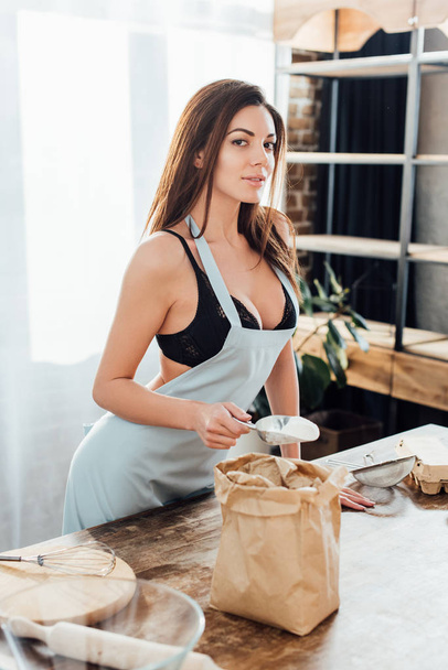 Sexy woman in underwear and blue apron with flour in paper bag in kitchen - Foto, Imagen