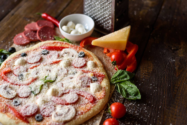 Сырая пицца с ингредиентами на деревянном столе
 - Фото, изображение