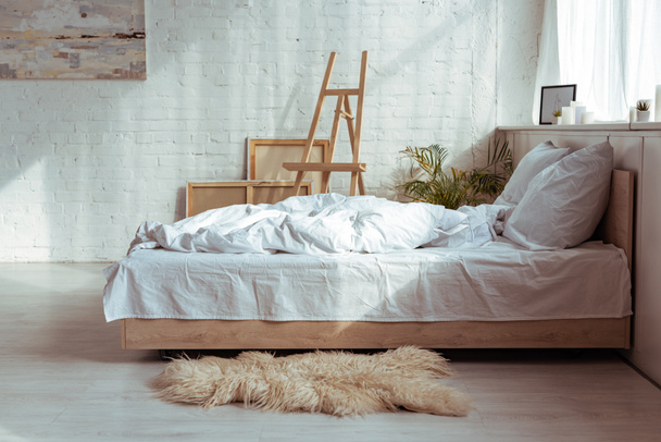 Schlafraum mit gemütlichem Bett, Kissen, Decke, Bildern und Staffelei  - Foto, Bild