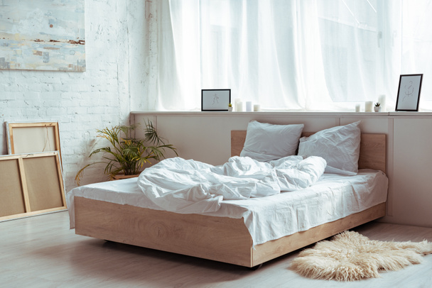 interior del dormitorio con acogedora cama, almohadas, manta, fotos y planta
  - Foto, Imagen