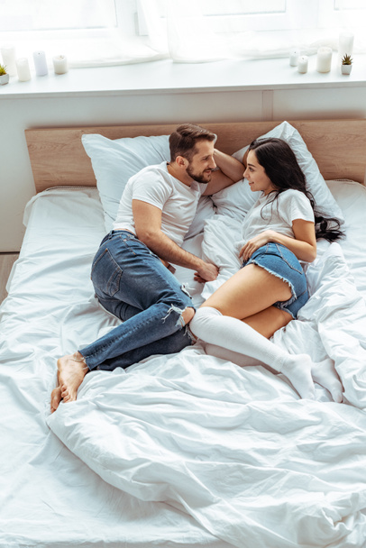 handsome man and beautiful and smiling woman in white t-shirt looking at each other in bedroom  - Fotó, kép