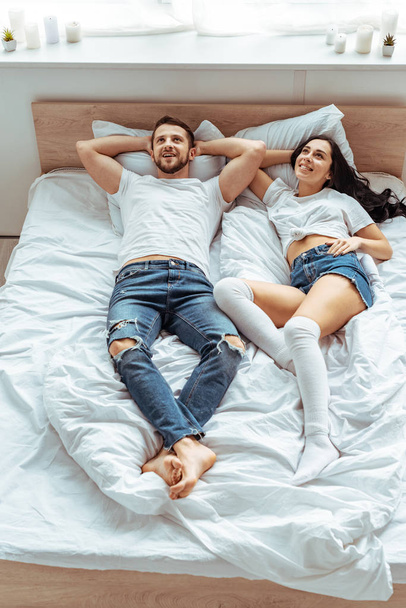hombre guapo en jeans y mujer hermosa y sonriente en camiseta blanca mirando hacia arriba en el dormitorio
  - Foto, imagen