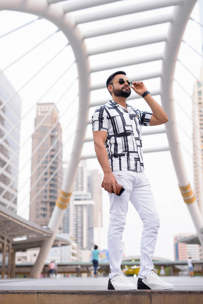 Full body shot of bearded Indian man with sunglasses thinking in the city - Foto, imagen