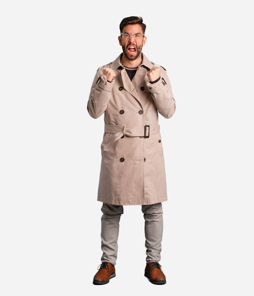 Young man wearing trench coat screaming very angry and aggressive - Foto, Imagem