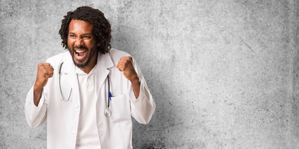 Bonito médico afro-americano muito feliz e animado, levantando os braços, celebrando uma vitória ou sucesso, ganhar na loteria
 - Foto, Imagem