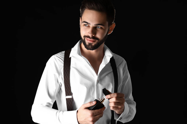Handsome man with bottle of perfume on dark background - Foto, afbeelding