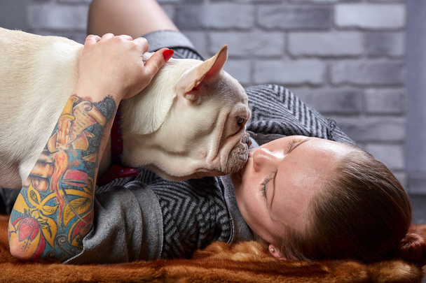 Französische Bulldogge auf den Händen seines Herrchens. Man hat das Gefühl, das Mädchen liebt ihr Haustier und umarmt und küsst es fest. - Foto, Bild