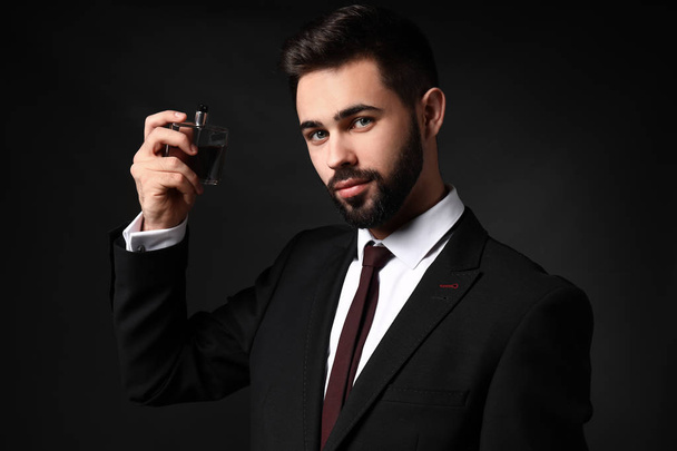 Knappe man met fles parfum op donkere achtergrond - Foto, afbeelding