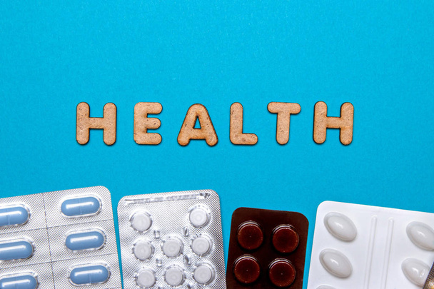 Pills with wooden letters form the word health on a blue background. Top view - Фото, изображение