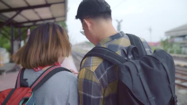 Asian plecak para w Train Station, młody słodki para turystyczny Backpacker przy pomocy zdejmowany telefon patrząc i kierunek mapy u ich podróż w Tajlandia. Lifestyles para relaks i koncepcja podróży. - Materiał filmowy, wideo