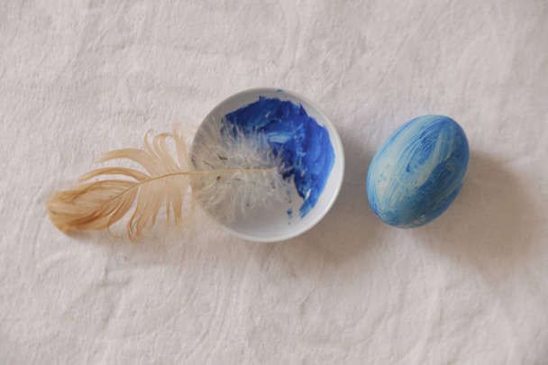 Uovo di Pasqua blu sul tavolo accanto alla vernice e piuma, dolore
 - Foto, immagini