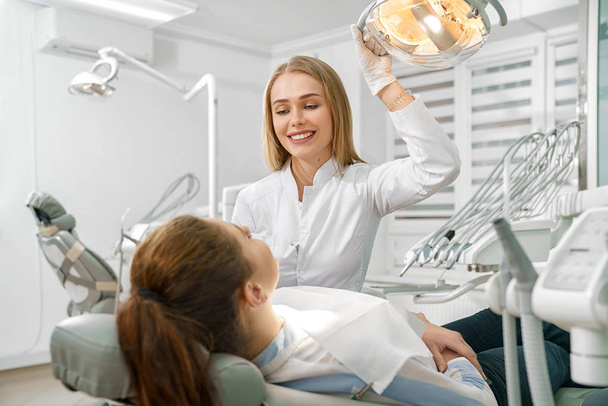 Female dentist talking with patient lying on dental chair - Fotoğraf, Görsel