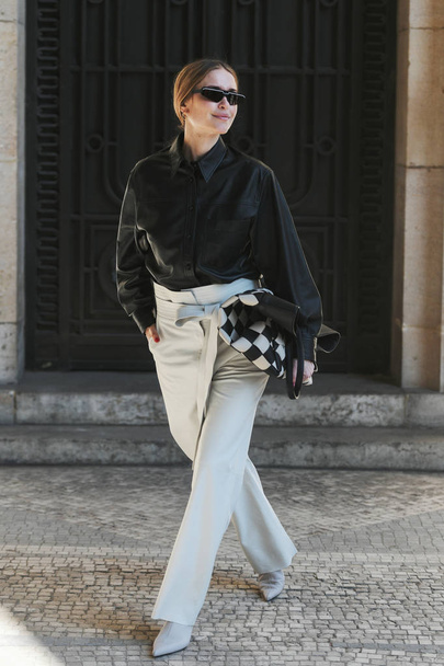 Paris, France - February 27, 2019: Street style outfit -  Woman wearing black leather shirt, white flared pants, a black and white checked bag, sunglasses before a fashion show during Paris Fashion Week - PFWFW19 - Photo, image