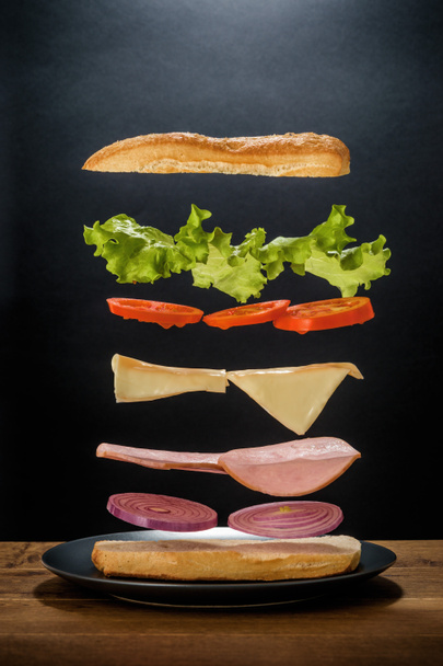 Componentes flotantes de delicioso andwich sobre el fondo negro
 - Foto, imagen