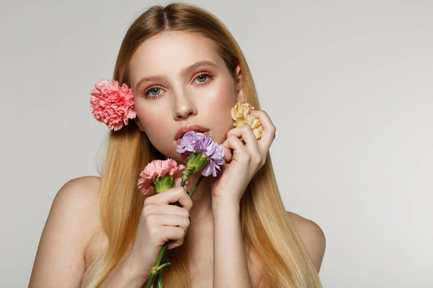 Playful and sexy portrait of pretty cheerful woman with spring flowers near her face - Photo, Image