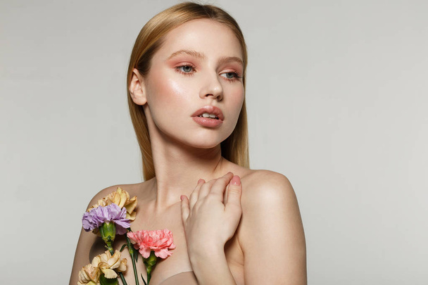 Encantador modelo femenino con piel perfecta sosteniendo flores en la mano
 - Foto, Imagen