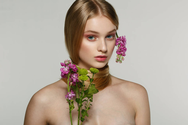 schöne junge weibliche Modell mit blauen Augen, perfekte Haut mit Blumen auf der Schulter - Foto, Bild