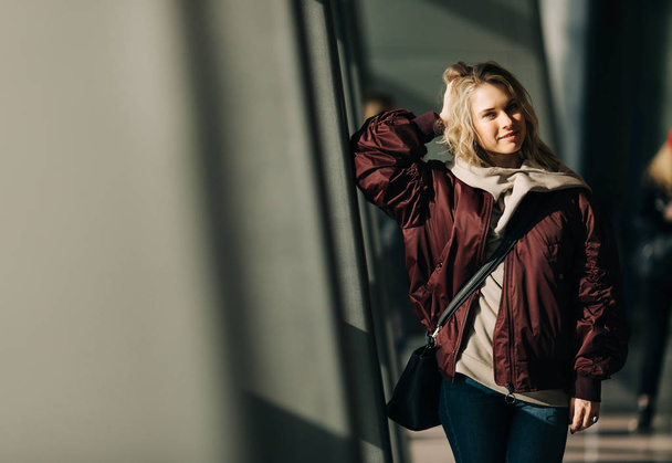 Photo of blonde in jacket standing against windows - Foto, Imagen