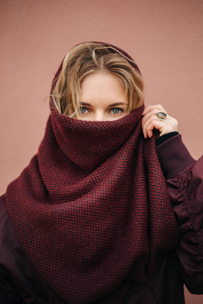 Photo of young blonde woman with closed scarf face on background of wall. - Foto, afbeelding