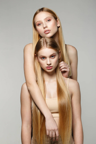 Two blonde beautiful girls with long hair looking at camera in the studio on a bright background - Fotoğraf, Görsel