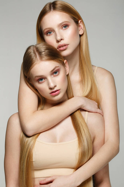 Twee mooie zuster tweeling meisjes met dezelfde blonde lange haren en perfecte huid - Foto, afbeelding