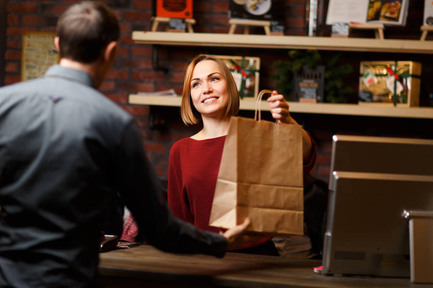 Picture of woman seller with paper bag and man from behind - Foto, imagen