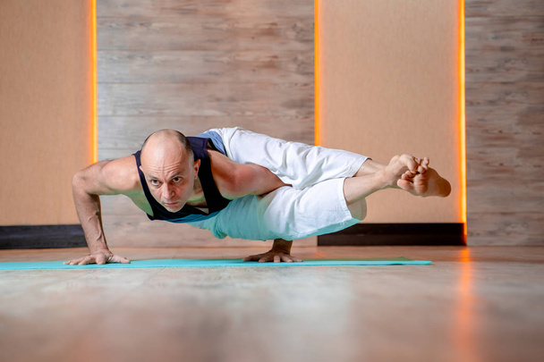 Athlete man practices yoga while standing on hands on blue mat . - 写真・画像